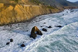 The Pacific Ocean washes against the rugged shoreline of northern California on a beautiful day. The Pacific Coast Highway runs along this area