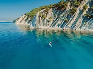 Paddle boarding in Mediterranean sea with mountain coastline. Aerial view