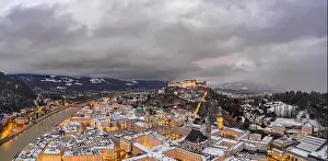 Salzach Prints: Panoramic aerial drone shot view of snowy Salzburg old town and Hohensalzb with city lights on during winter dusk hour