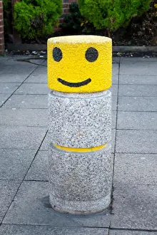 British English Prints: A pavement bollard painted with a yellow and black Smiley Face