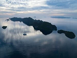 April Collection: A peaceful sunrise illuminates dramatic limestone islands that rise from Raja Ampat's beautiful