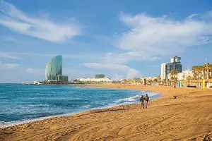Pedestrians walk along Barceloneta Beach in Barcelona with colorful sky at sunrise. Seafront, beach, coast in Spain. Suburb of Barcelona, Catalonia