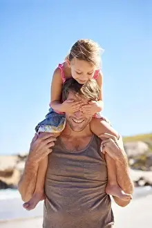 Blondie Prints: No peeking. A cute little girl covering her fathers eyes while hes giving her a piggyback ride at the beach