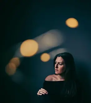Melancholy Prints: Pensive pretty woman in dark room with light bokeh surrounding her