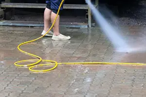 Shoe Prints: A person cleaning wet pavement with yellow hose spraying water