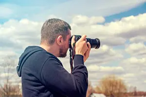 Backpacker Prints: Person taking picture by reflex camera. Man with black photo camera in warm summer day