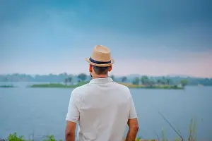 Contemplation Prints: A person wearing a hat stands by a tranquil lake surrounded by lush greenery