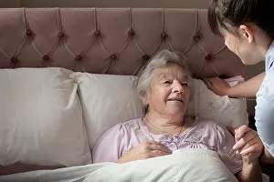 Tiredness Prints: Personal care assistant chatting to senior woman in bed