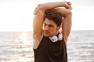 Satisfied Prints: Photo unshaven man in tracksuit with headphones doing exercise while working out at seaside in morning