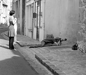 A photographer lying on the ground taking a low angle shot watched by his assistant in provincial France