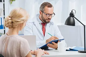 Professional Occupation Prints: physiotherapist in white coat making notes in notepad with female patient near by during appointment in clinic