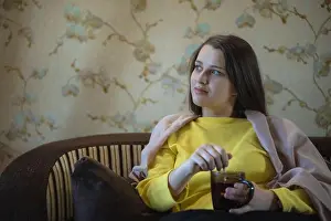 City Lights Prints: A picture of nice and thoughtful girl sits at sofa and drinks tea