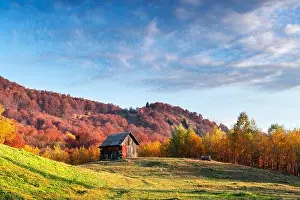 Picturesque autumn meadow with wooden house and red beech trees in the Carpathian mountains, Ukraine. Landscape photography