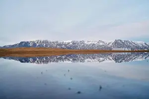 Immense Prints: Picturesque view of rough mount with snow reflecting in icy river under cloudy sky in Iceland