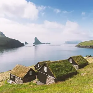 Picturesque view of tradicional faroese grass-covered houses in the village Bour. Drangarnir and Tindholmur sea stacks on background