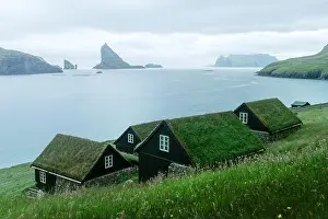 Picturesque view of tradicional faroese grass-covered houses in the village Bour. Drangarnir and Tindholmur sea stacks on background. Vagar island, Fa