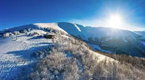 Wintersport Prints: Picturesque winter panorama of mountain hills covered with snow and fir trees on a sunny clear day with the sun