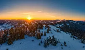 Picturesque winter panorama of mountain hills covered with snow and fir trees on a sunny clear day with the sun
