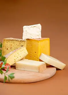 Delicatessen Prints: Pieces of assorted fresh cheese placed on wooden chopping board against brown background