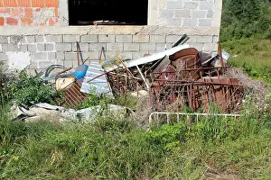 Garbage Prints: Pile of garbage and rusted metal left in nature next to unfinished brick house surrounded with high uncut grass
