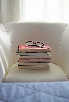 Spectacles Prints: a pile of hardback books and eyeglasses on a white armchair