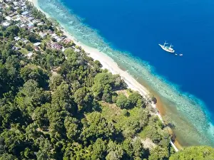 A Pinisi schooner sails along the edge of a dramatic coral reef in the Banda Islands of Indonesia. This region is high in marine biodiversity