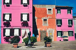 Siesta Prints: Pink and orange houses in an empty town square with public water fountain during off season in Burano island