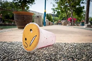 Polluted Prints: Plastic waste pollution- A disposed plastic drinking contain with a sad face lying on a street floor
