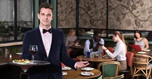 Tray Prints: Polite waiter holding tray at restaurant with customers behind him