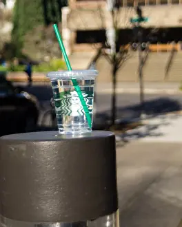 Polluted Prints: Portland Oregon United States. Starbucks glass with green straw full of water abandoned on the street