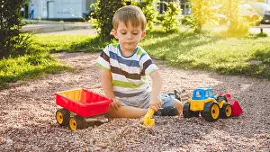 Early Spring Prints: Portrait of adorable 3 years old toddler boy playing with toy truck with trailer on the playground at park