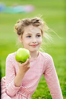 Preteen Prints: portrait of adorable smiling girl eating green apple while sitting on grass at park