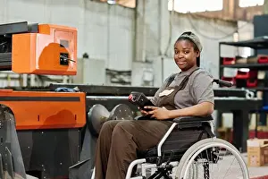 Workwear Prints: Portrait of African worker sitting in wheelchair with remote control to control the operation of machine at factory