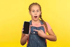 Shocked Prints: Portrait of amazed little girl with braid in denim overalls pointing at screen mock up