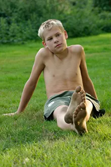 Preteen Prints: portrait of a barefoot young boy with dirty feet sitting in the grass
