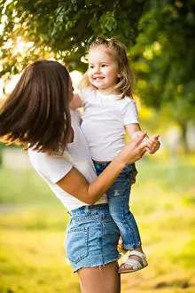 Cuddle Prints: Portrait of beautiful mother with love hugging her precious daughter in bright yellow sunlight in the park