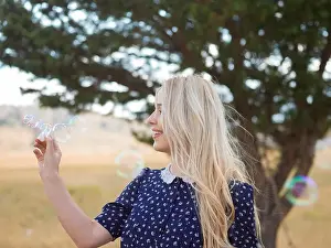 Portrait of a beautiful young woman blowing soap bubbles in the park on a sunny summer day