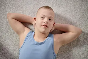 Disability Prints: Portrait of Boy Child with Down Syndrome Relaxing on Carpet Smiling