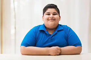 Portrait of a chubby boy sitting with his hands on the table. (Obesity)
