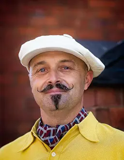 Forties Prints: Portrait close up of isolated handsome man with waxed moustache & newsboy cap looking dapper in 1940s dress