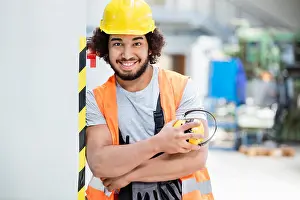 20 24 Years Prints: Portrait of confident male worker in protective clothing holding ear protectors at factory