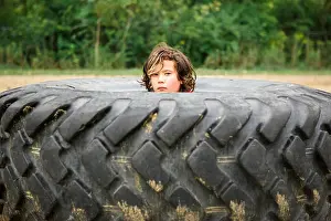 Mixed Race Prints: Portrait of cute boy peeking through dirty tire against plants