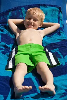 Lying Down Prints: Portrait of a cute little boy in swimsuit lying down on blue towel