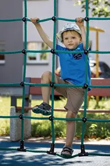 Playtime Prints: Portrait of cute smiling boy climbing up the rope net he look at camera