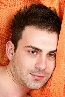 Brown Eyes Prints: Portrait of a dreamy young man with brown eyes and brown hair over an orange pillow