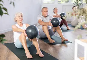 Gymnastic Prints: Portrait of elderly people doing exercises for press with pilates ball during group class in fitness studio