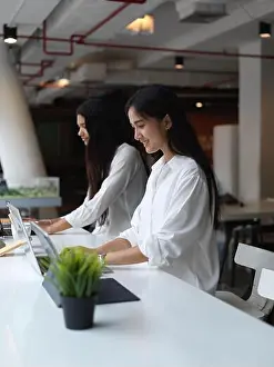 Female Friends Prints: Portrait of female students concentrating on digital tablet while sitting beside each other in co working space