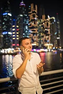 Office Worker Prints: Portrait of handsome man talking on the phone in the night light on skyscrapers background