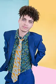 Suits Prints: Portrait of a handsome mixed race young man wearing a blue suit and colourful shirt and tie stands in front of a yellow
