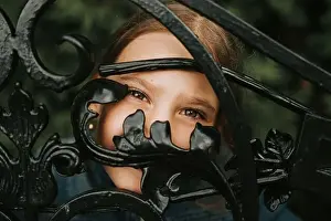 portrait happy candid eight year old caucasian kid girl brown eyes peeking through of abstract metal shapes in nature